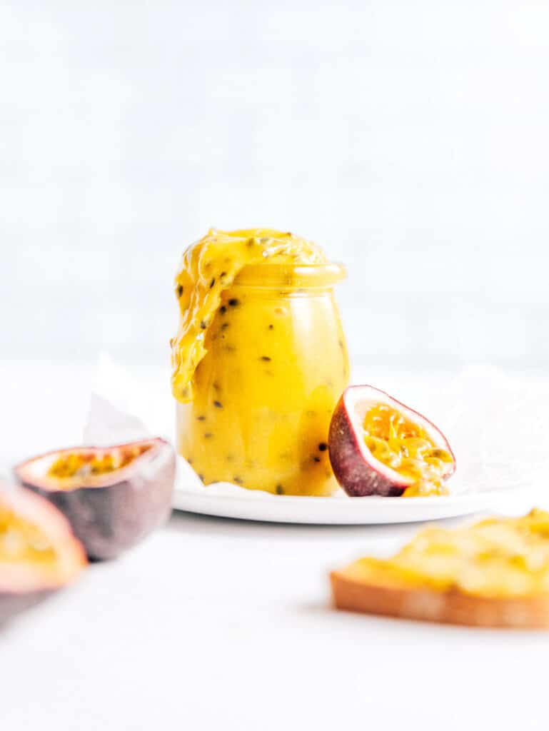 Passion fruit curd in a small glass jar next to cut open fruit.
