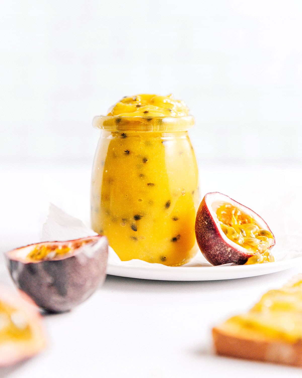 Passion fruit curd in a small glass jar next to cut open fruit.
