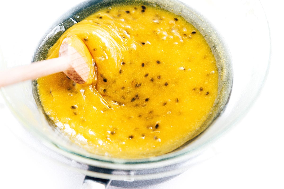 A wooden spoon stirring passion fruit curd in a double boiler.