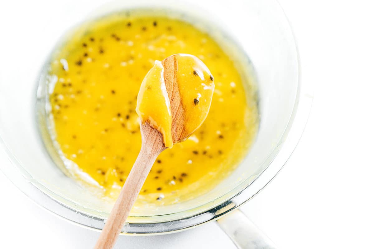 A wooden spoon with a scoop of passion fruit curd.