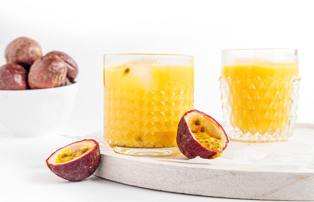 Two glasses of homemade passion fruit juice next to cut open passion fruit.