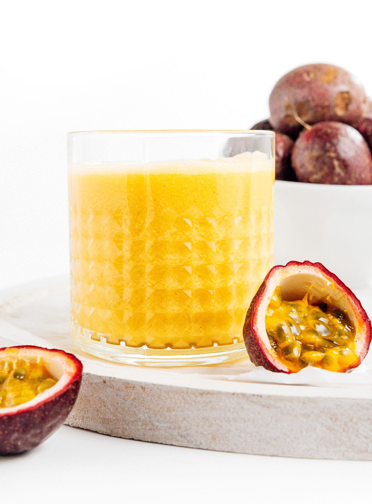 A small glass of homemade passion fruit juice next to cut open passion fruit.