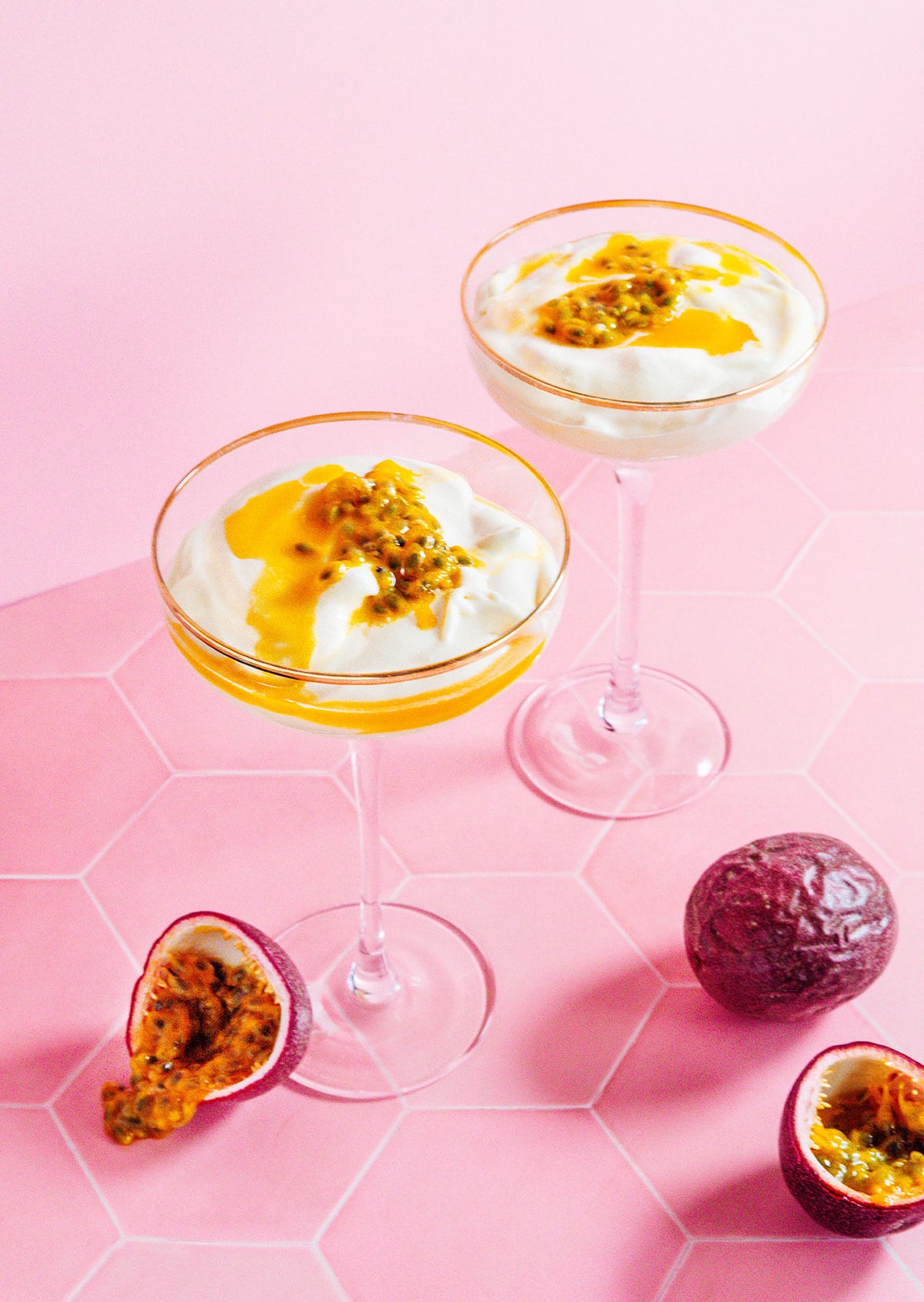 Two martini glasses of passion fruit mousse with whole passion fruit on the counter.