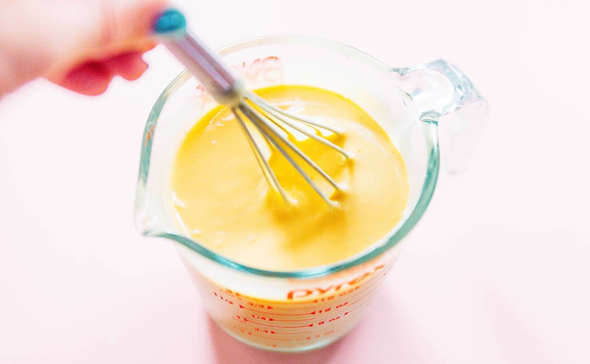 A hand whisking passion fruit puree and condensed milk in a glass measuring cup.