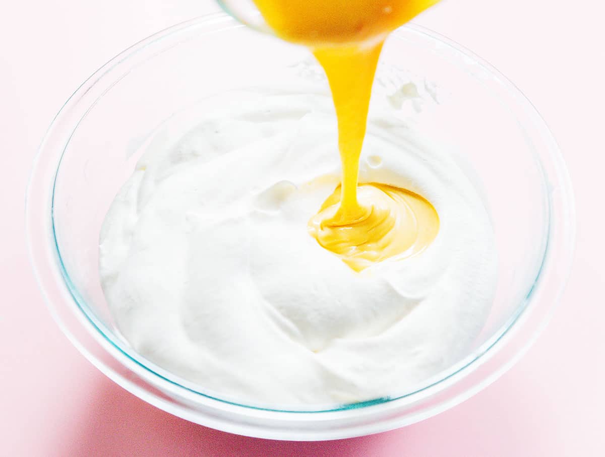 Passion fruit puree being poured into a glass mixing bowl of whipped cream.
