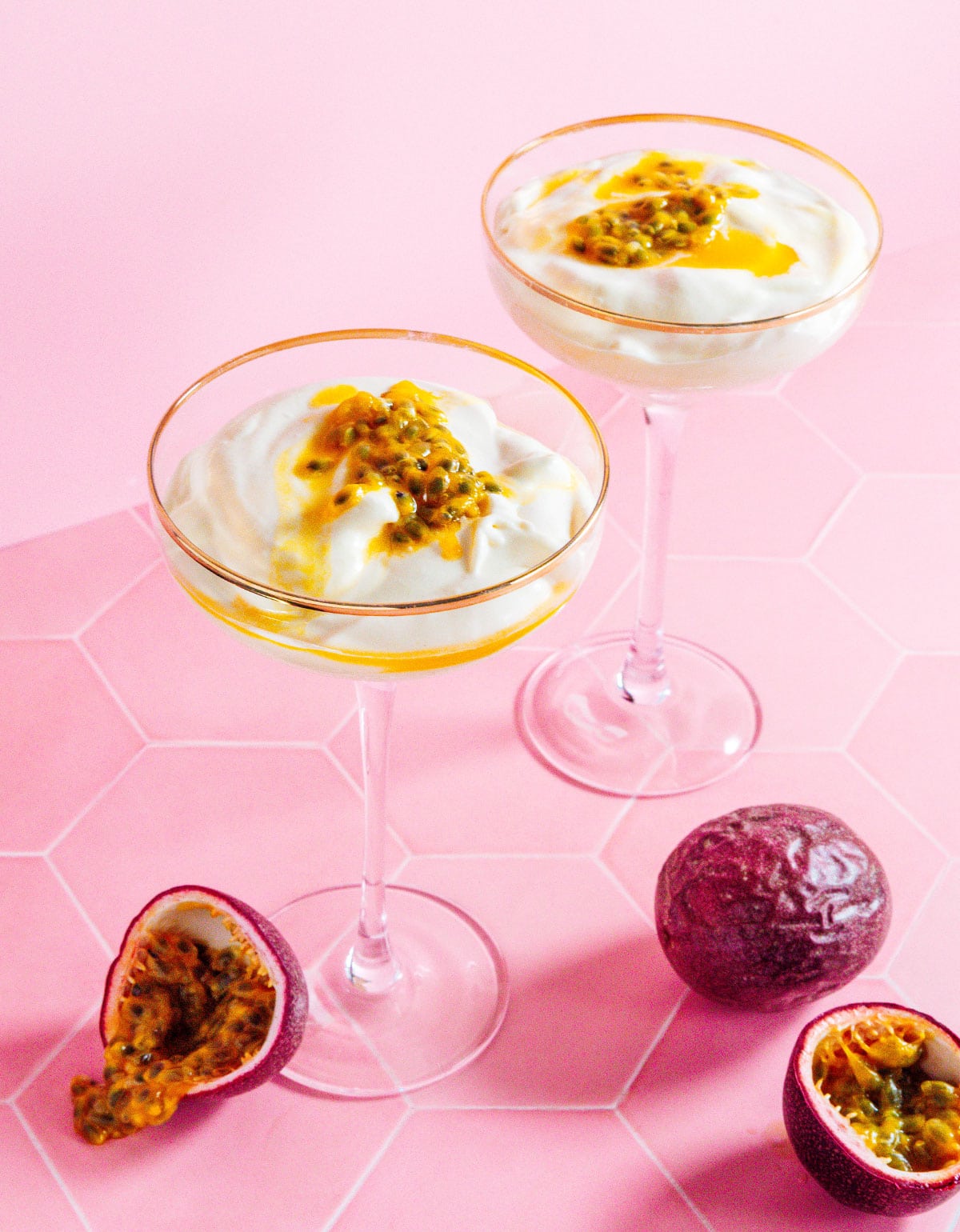 Two martini glasses of passion fruit mousse with whole passion fruit on the counter.