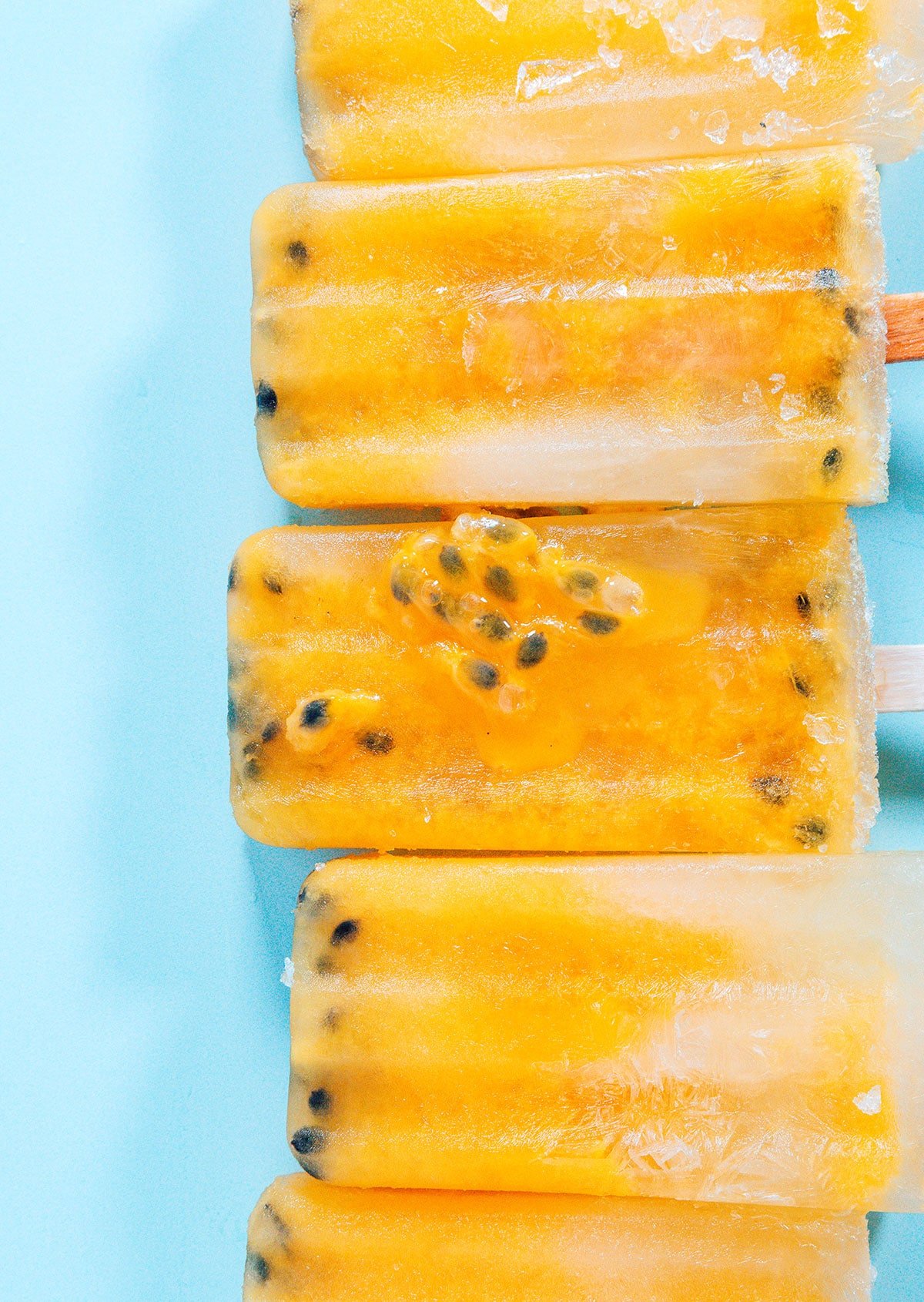 passion fruit popsicles lined up horizontally on a blue background.