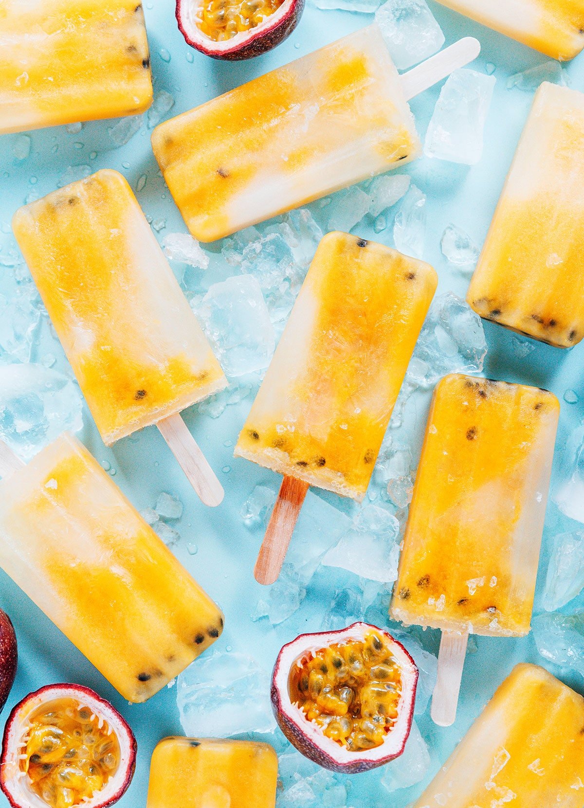 Popsicles, ice, and cut open passion fruit laid flat on a blue background.