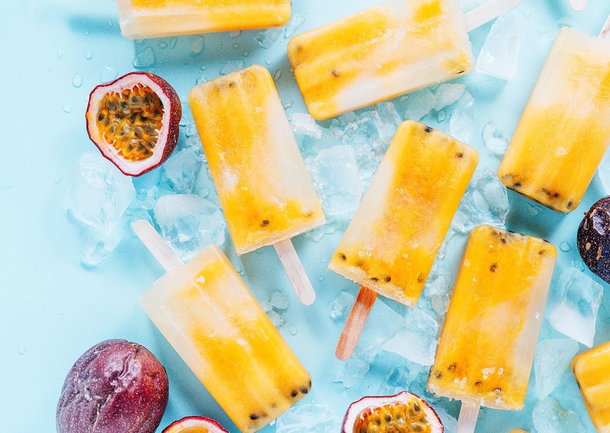 Popsicles, ice, and passion fruit cut open on a blue background.
