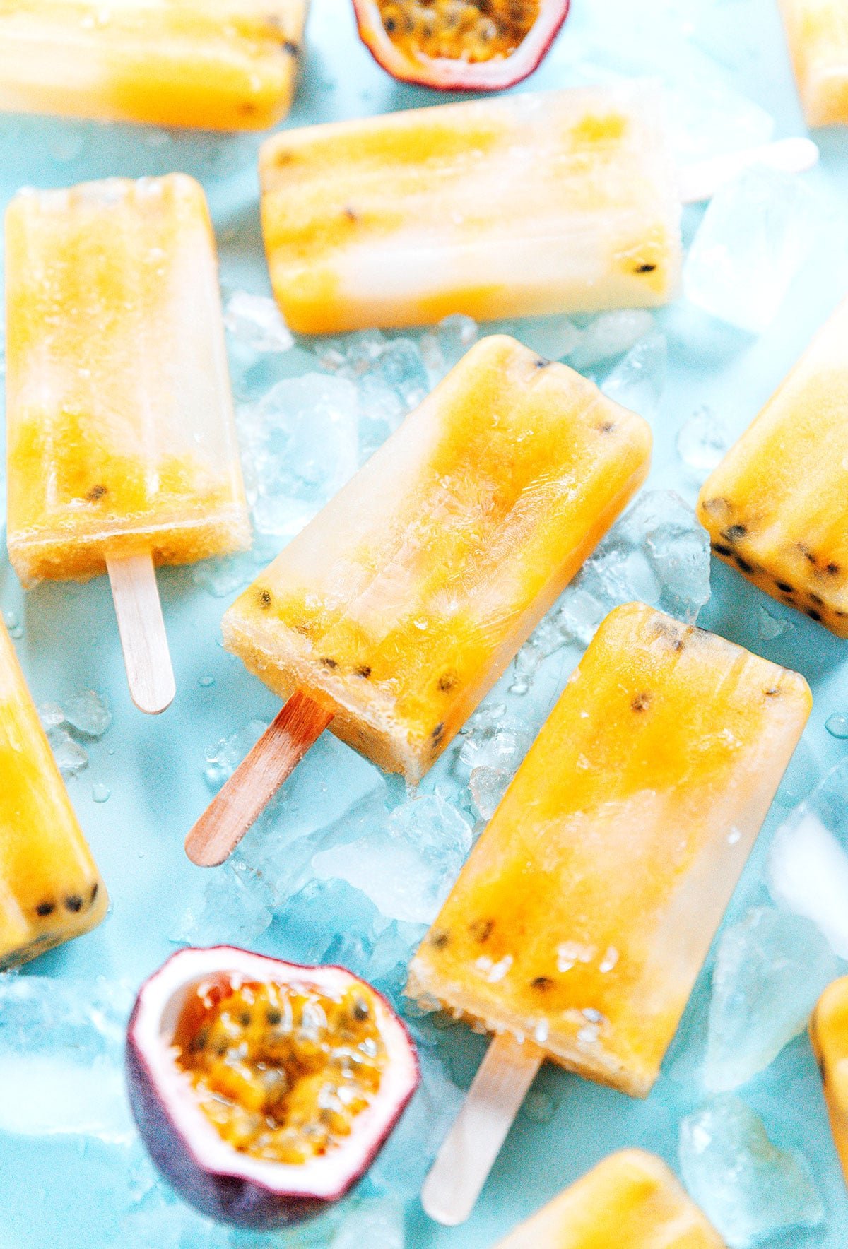 Popsicles, ice, and cut open passion fruit laid flat on a blue background.