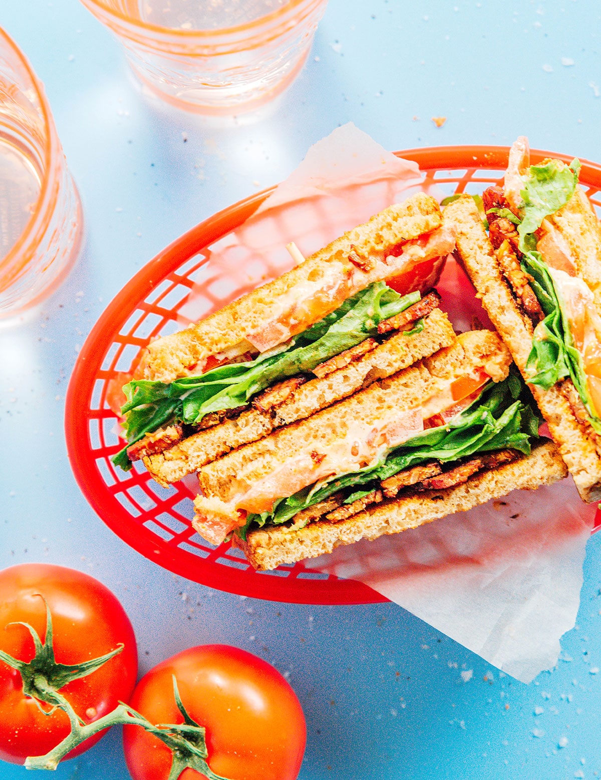 Three vegan BLT sandwich halves in a red plastic basket.