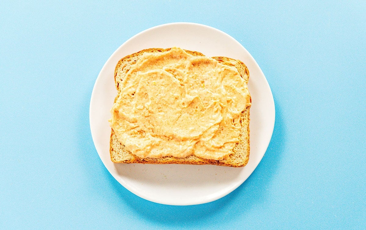 Spicy vegan mayo spread on a slice of toast on a small white plate.