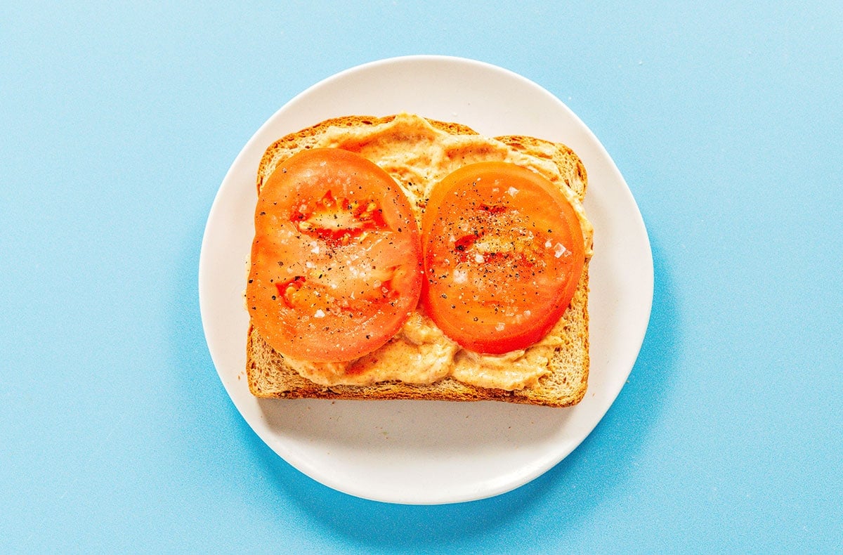 Tomato slices and spicy mayo layered on a slice of toast on a white plate.