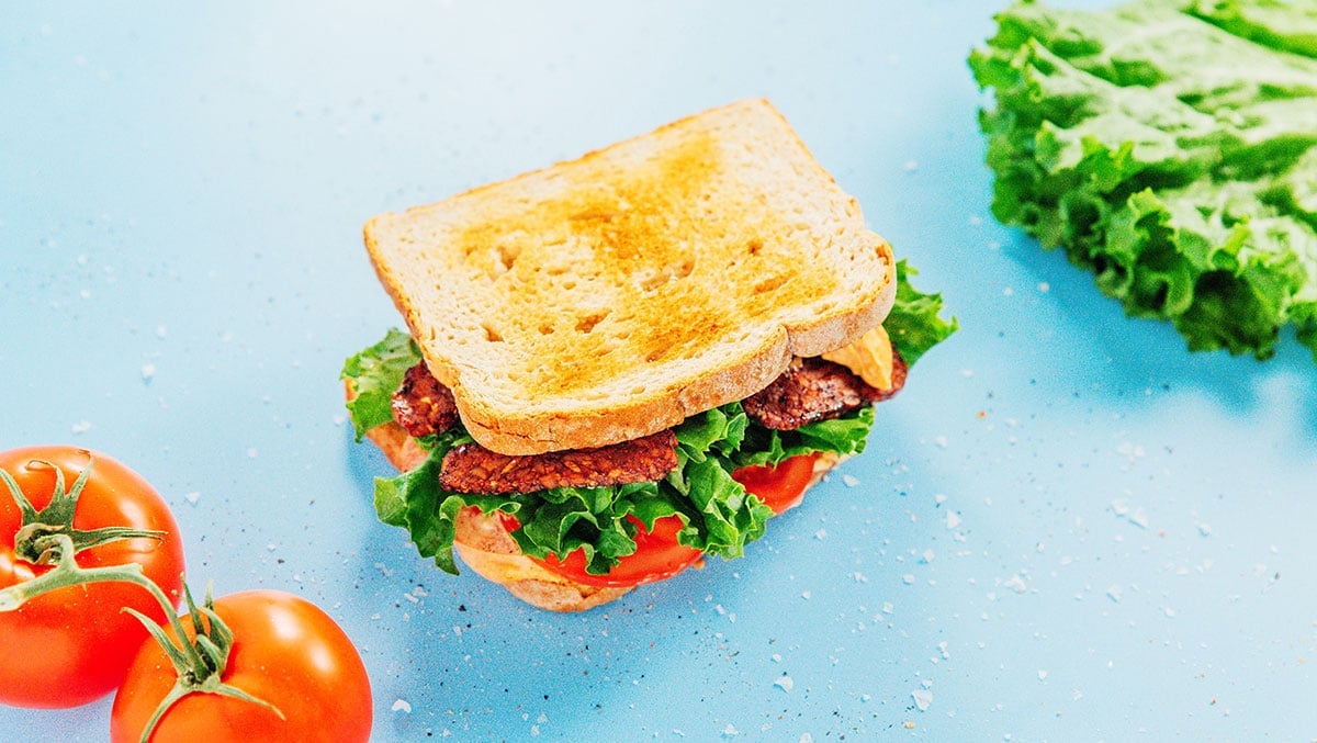 A vegan BLT toasted sandwich on a blue surface.