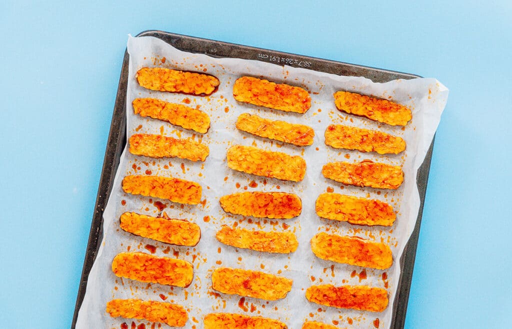 Bacon-flavored tempeh slices on a parchment lined baking sheet.