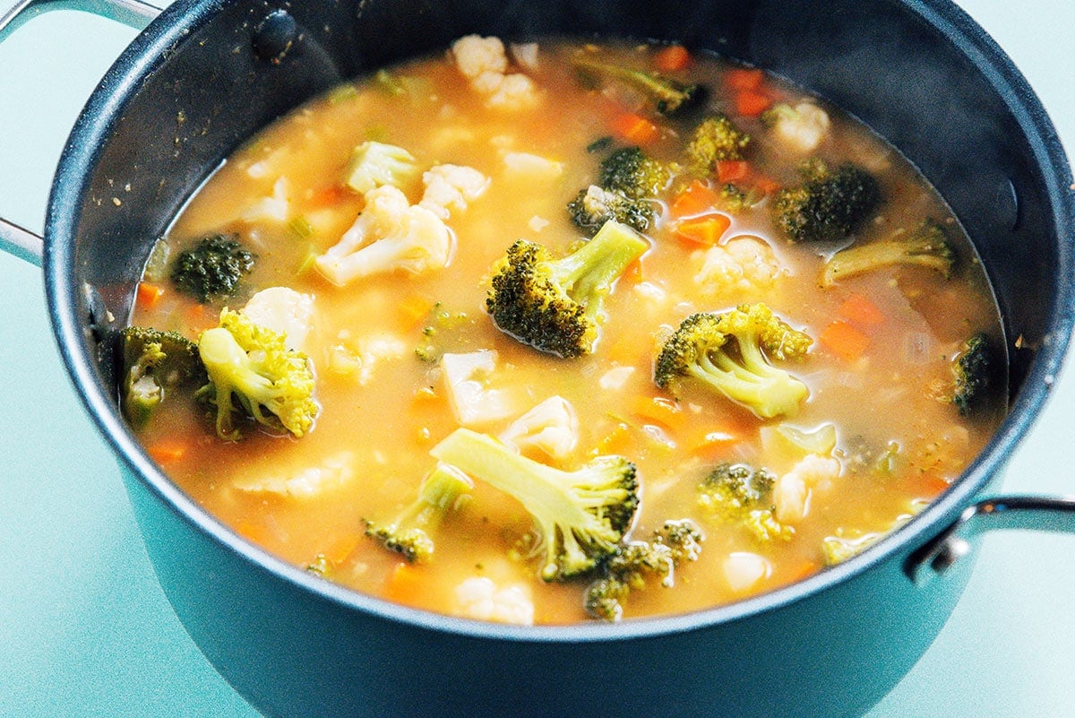 Broccoli and cauliflower floating in a stockpot of broth.