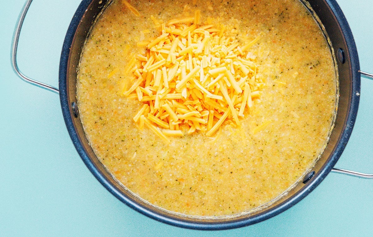 Shredded cheese on top of a pot of pureed veggie soup.