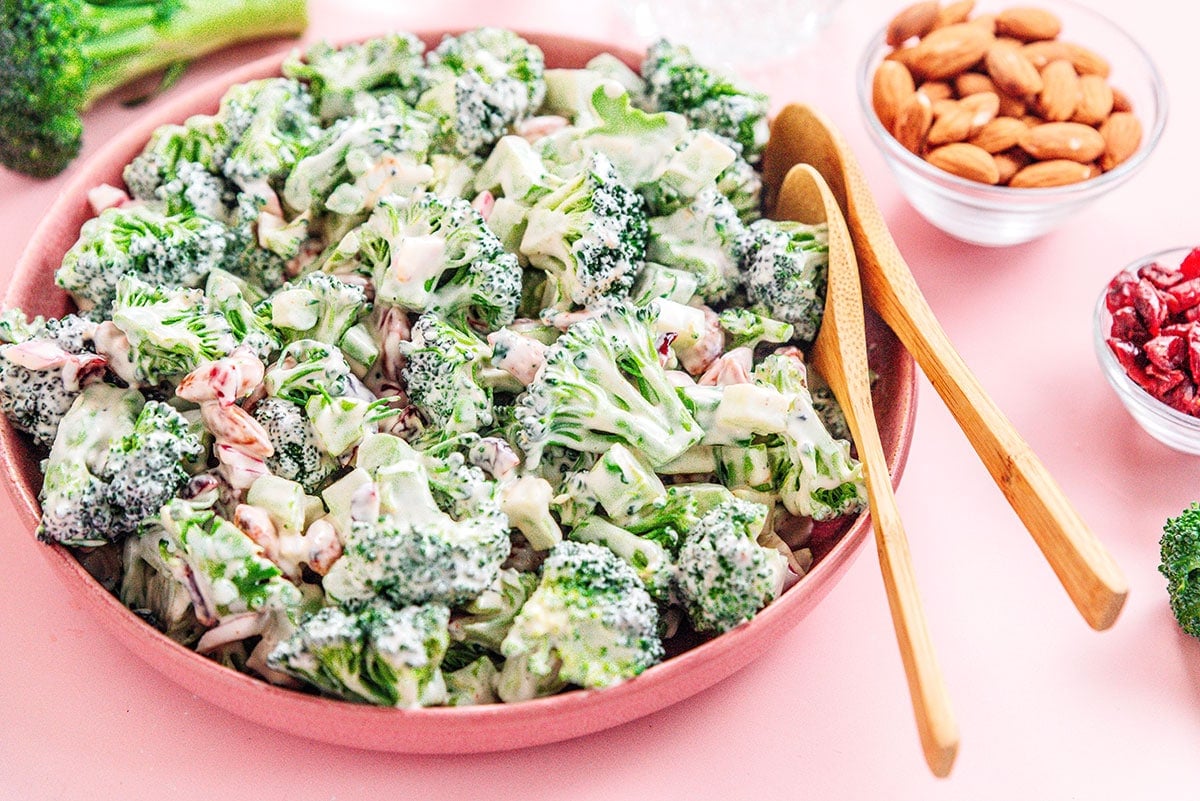 Large pink bowl of broccoli salad with wooden salad servers.