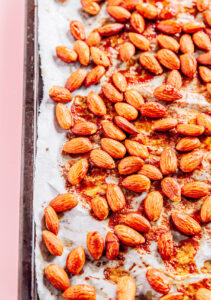 Roasted almonds coated in seasoning on a parchment-lined baking sheet, perfect for adding crunch to your favorite broccoli salad.