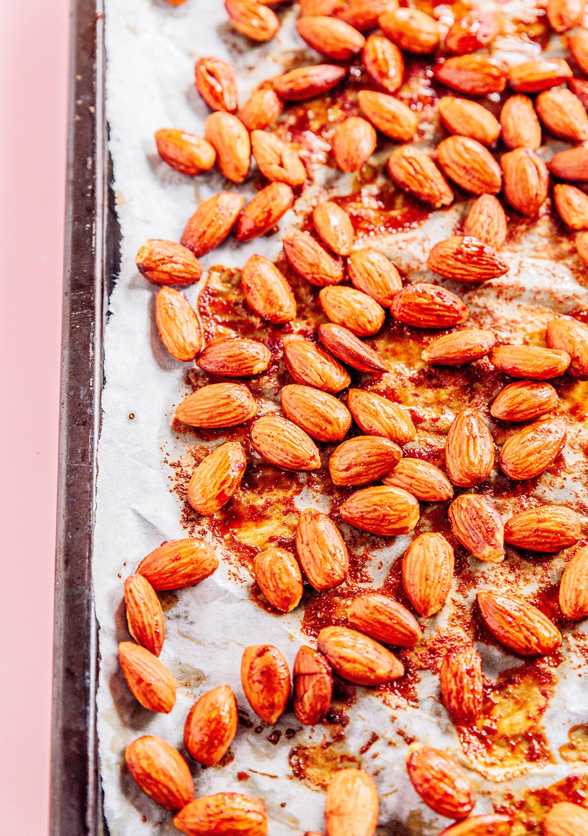 Almonds coated in smoky marinade on a parchment lined baking sheet.