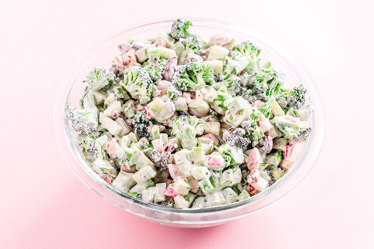 Broccoli salad mixed with dressing in a glass mixing bowl.