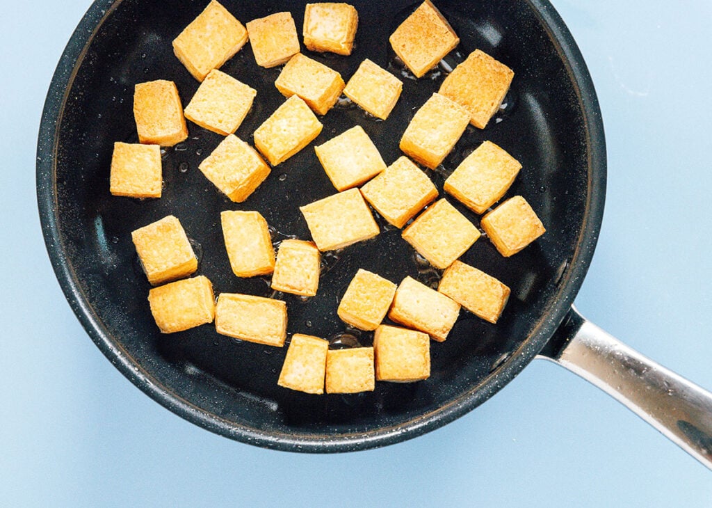 Tofu cubes being browned in a skillet.