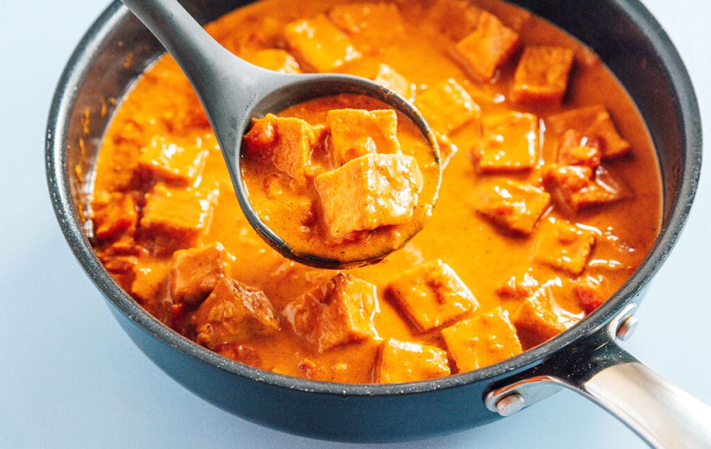 A ladle with a scoop of curried tofu over a full pot.