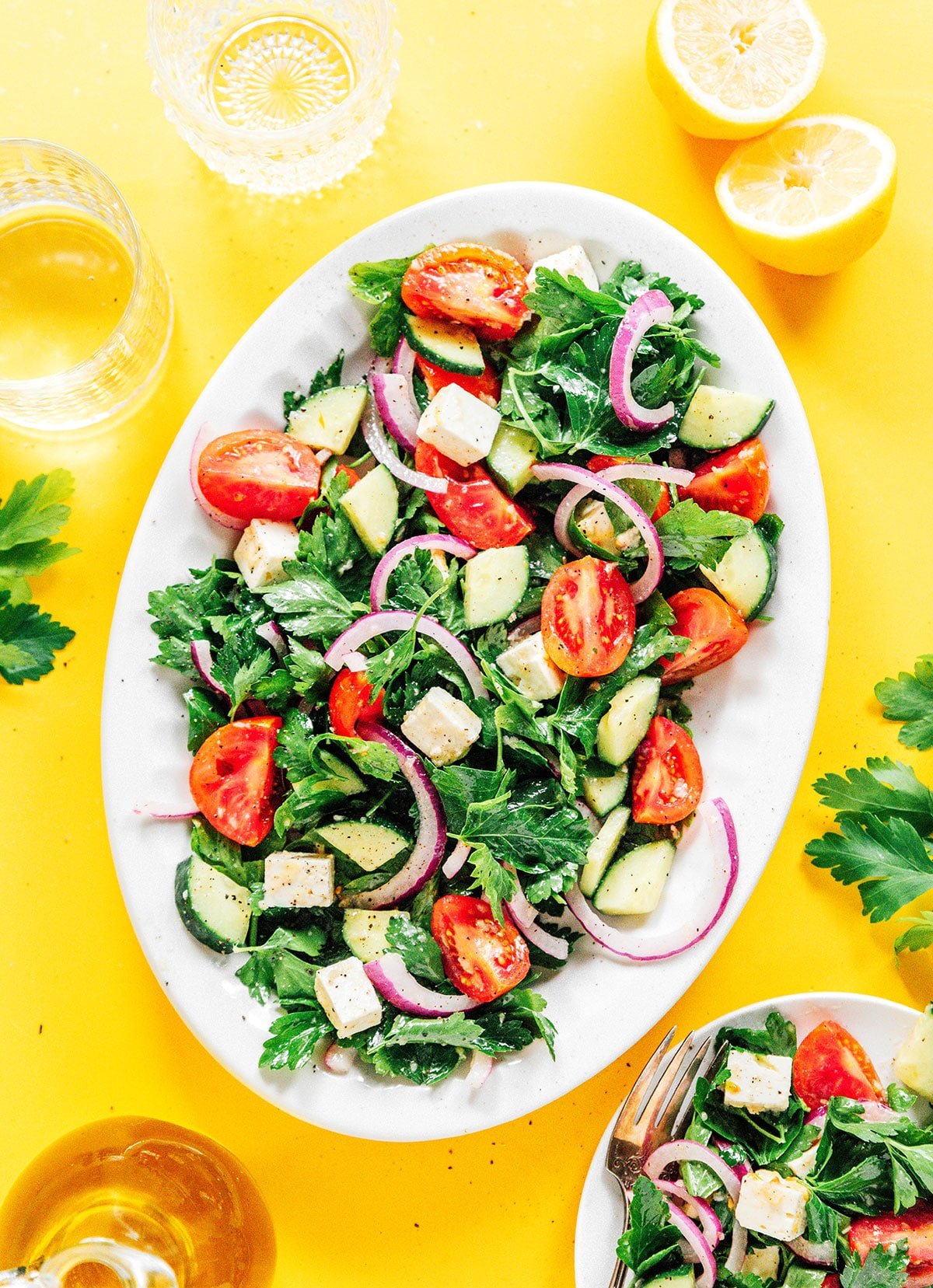Parsley salad with tomatoes, cucumber, red onions, and dressing on a white serving plater on a yellow background.
