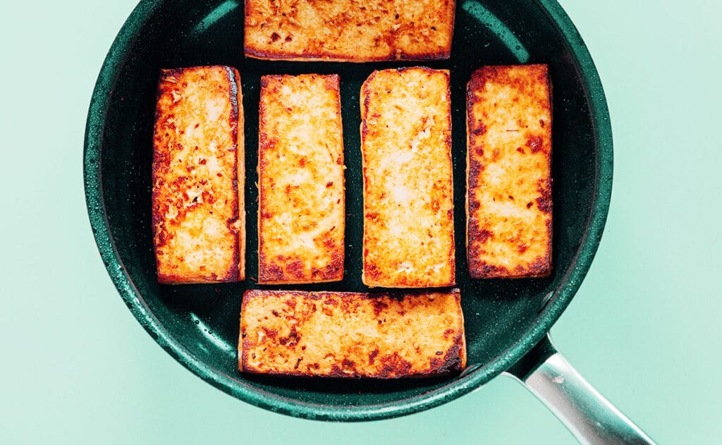 Tofu slabs crisping up in a nonstick skillet.