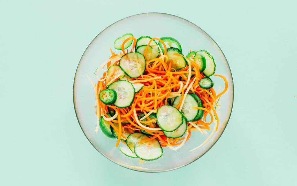 Julienned carrots and thinly sliced cucumber in a glass mixing bowl.