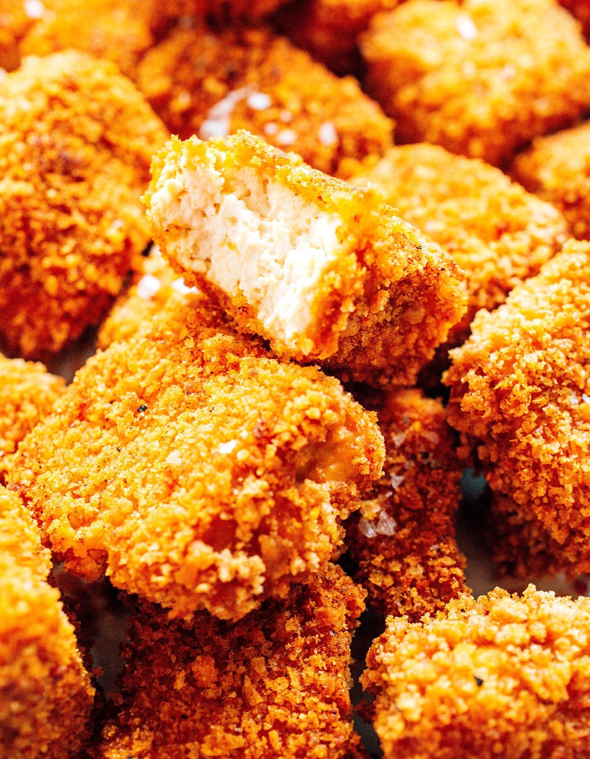 A pile of breaded tofu nuggets with one missing a bite.