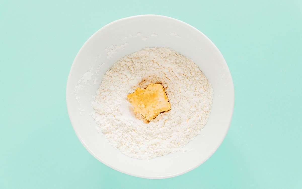 A marinated tofu nugget in a white bowl of flour.