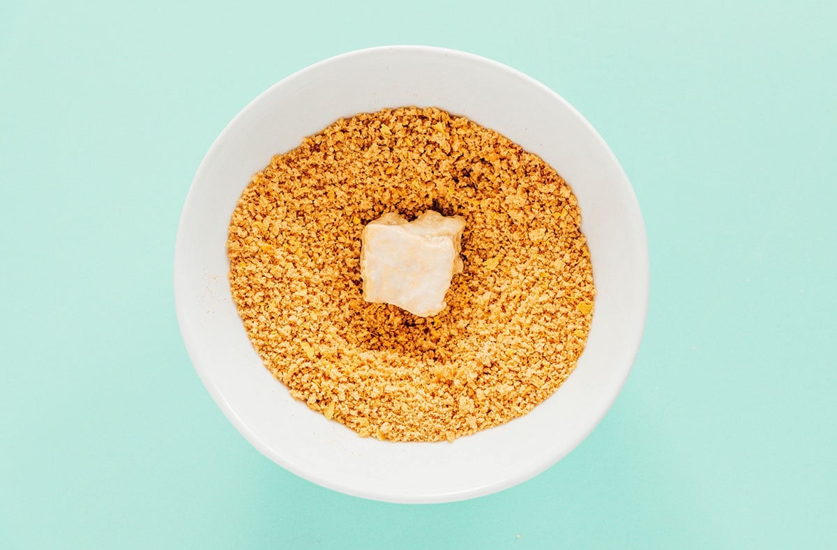 A tofu nugget being dredged in a small white bowl of panko.