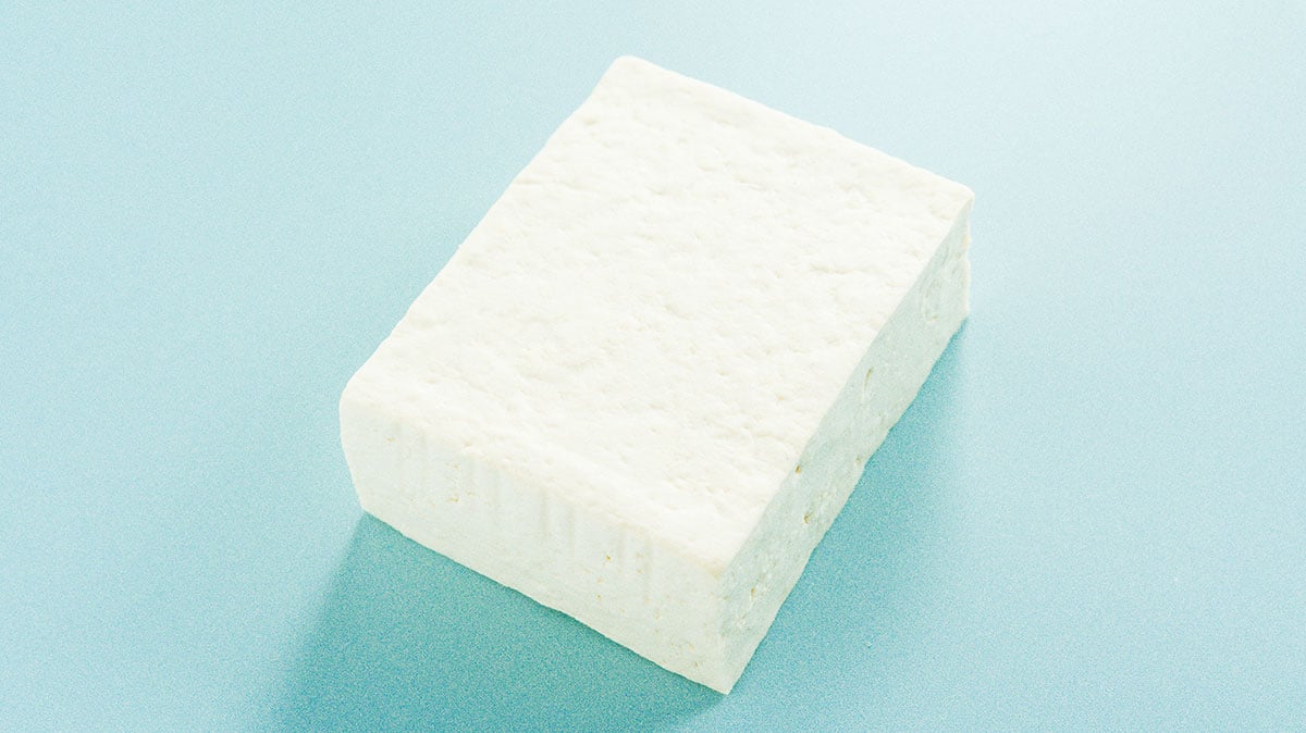 A block of firm tofu on a light blue background.