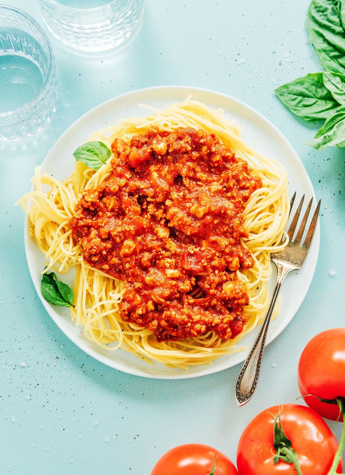 A fork in vegan spaghetti bolognese in a large white platter.