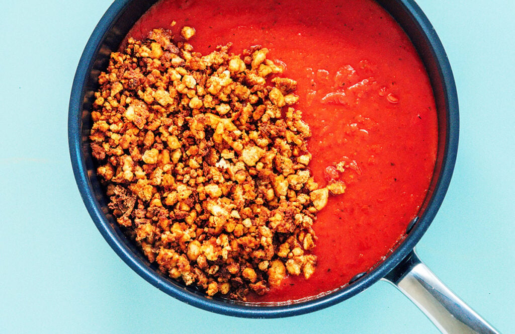 Seasoned and baked tofu crumbles in a pot of tomato sauce.