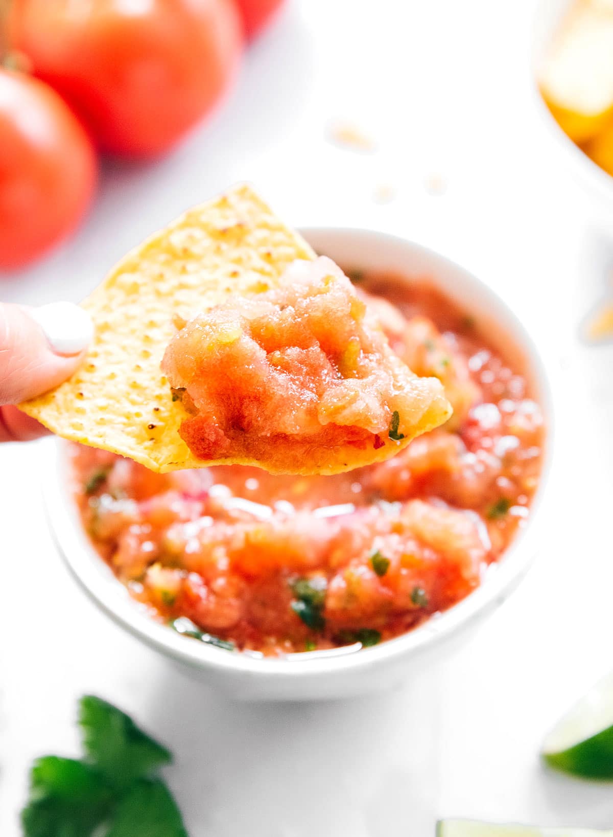 A chip being dipped into a small white bowl of blended salsa.