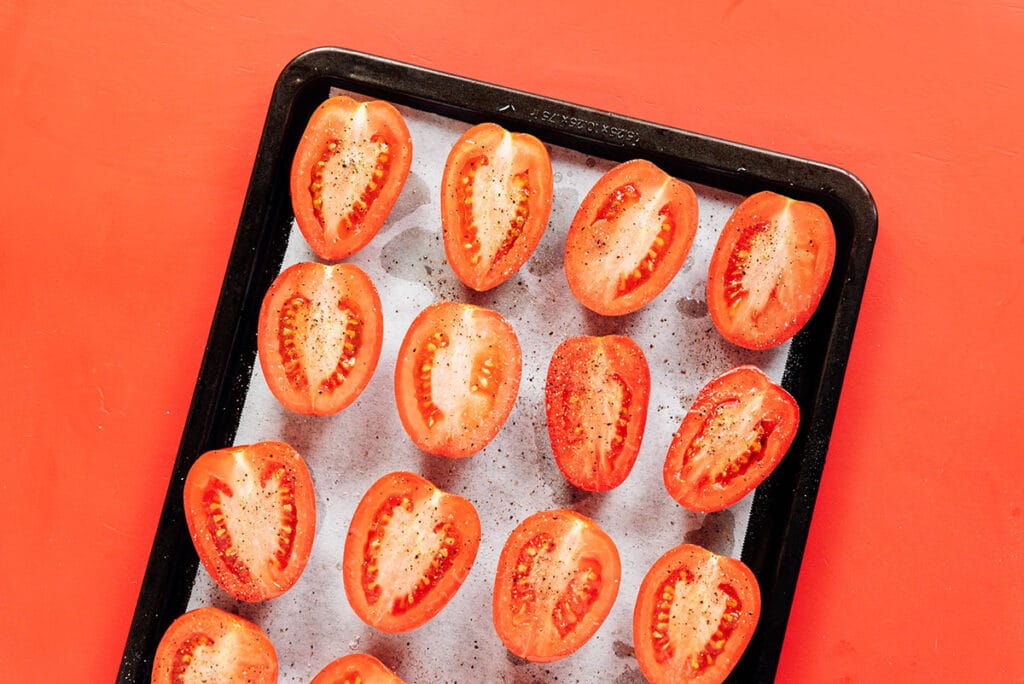 Roma tomatoes sliced half way and placed on a lined baking tray with salt and pepper.