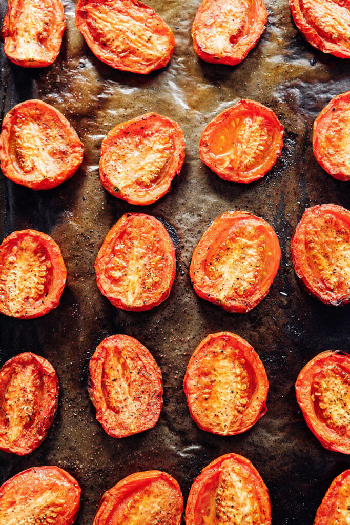 Roma tomatoes slightly shriveled and chared on a lined baking tray after baking.