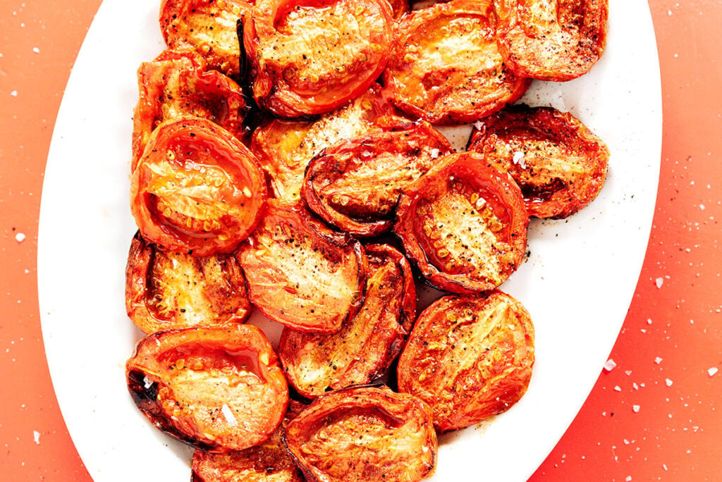 Fire roasted tomatoes on a white plate with black char marks and a slight shine from the oil.