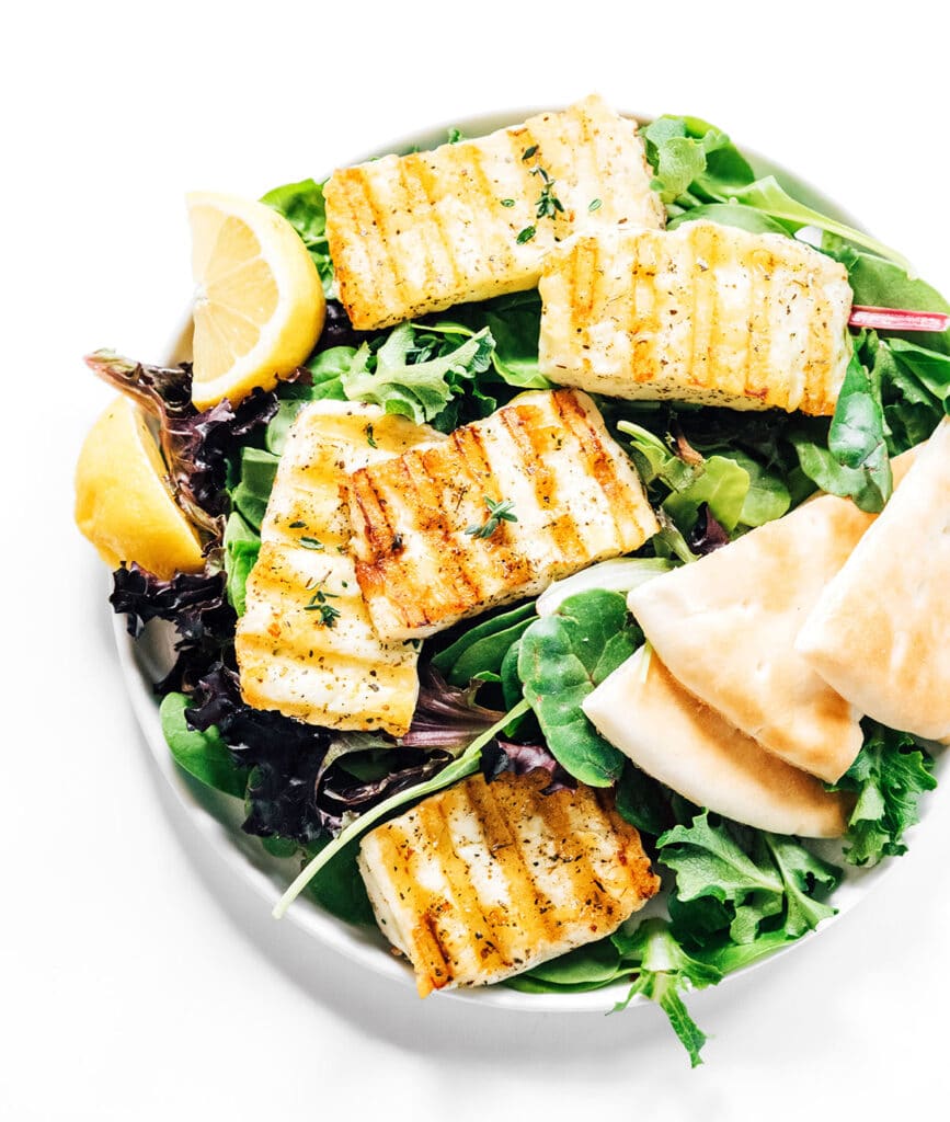 Grilled halloumi cheese on a white plate with salad and pita bread