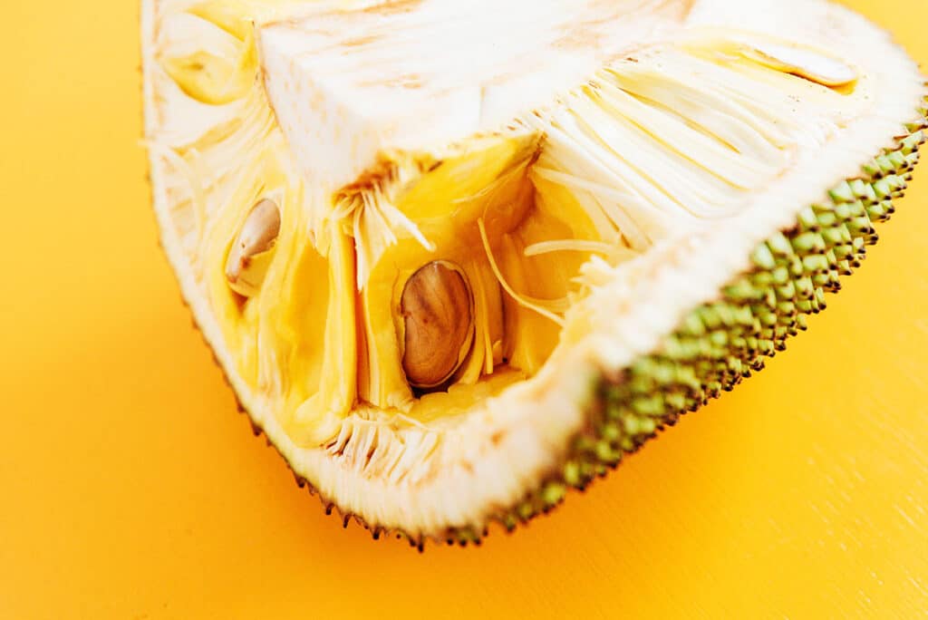 A sliced open jackfruit with the seeds  and bumpy surface visible.