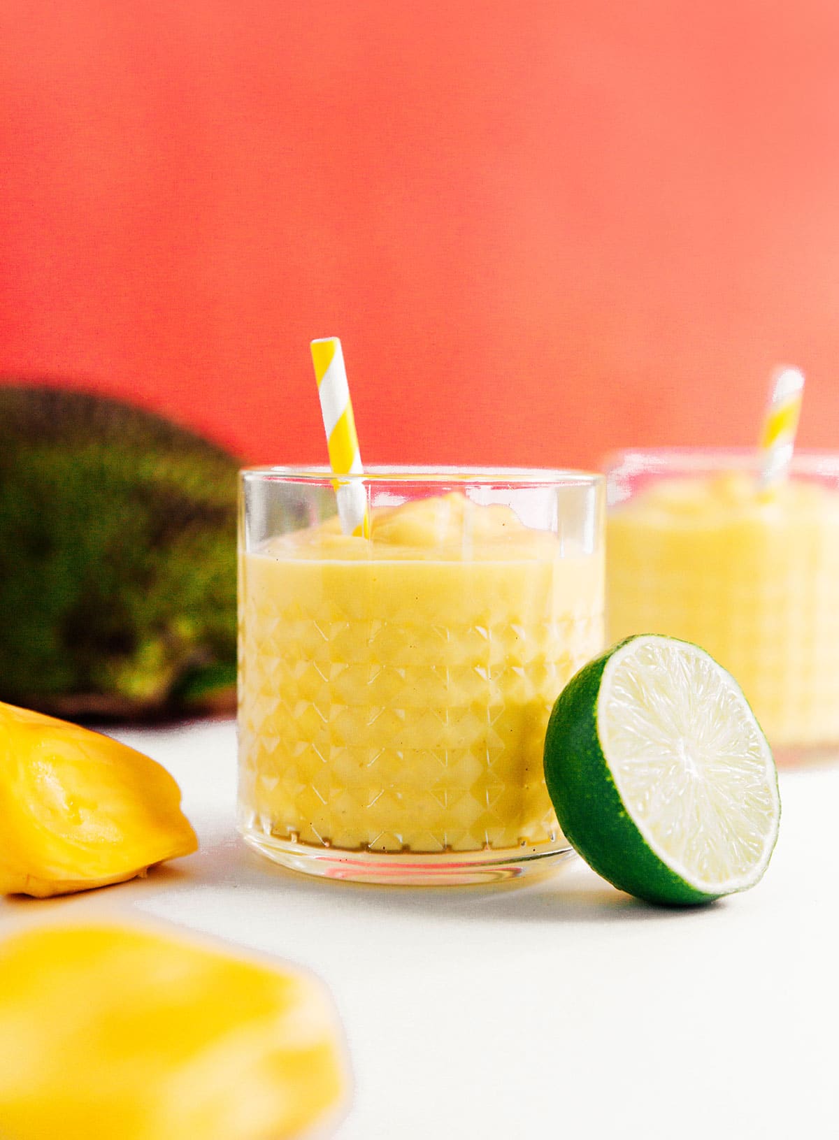 Two rocks glasses filled with jackfruit smoothies and yellow striped straws.