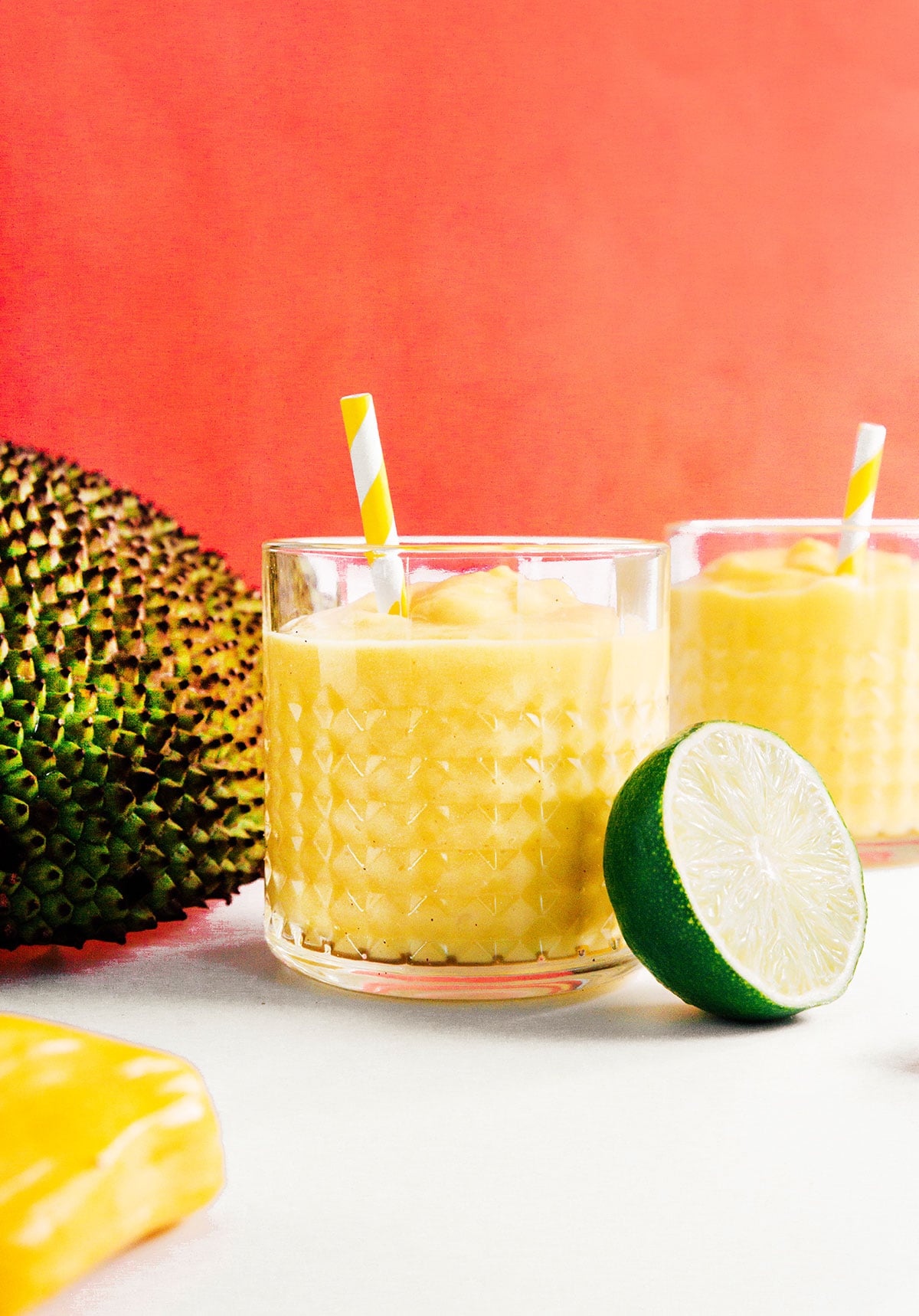 Two rocks glasses filled with jackfruit smoothies and yellow striped straws.
