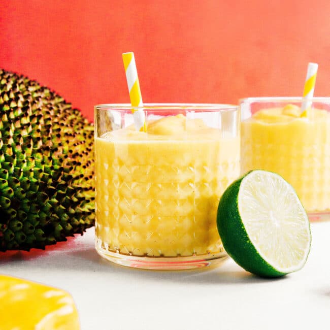 Yellow jackfruit smoothie in a glass with a yellow striped straw
