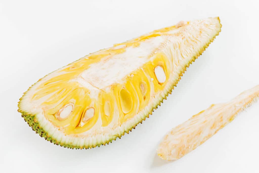 Bright yellow jackfruit cut open into a quarter with the thick middle removed and the bulbs exposed.