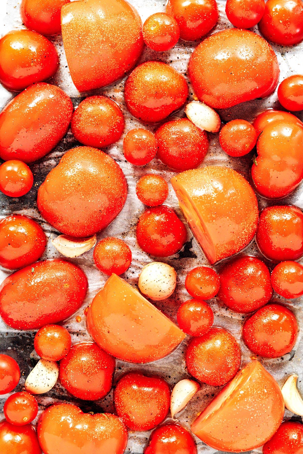 A sheet pan with garlic cloves and halved tomatoes of all sizes.