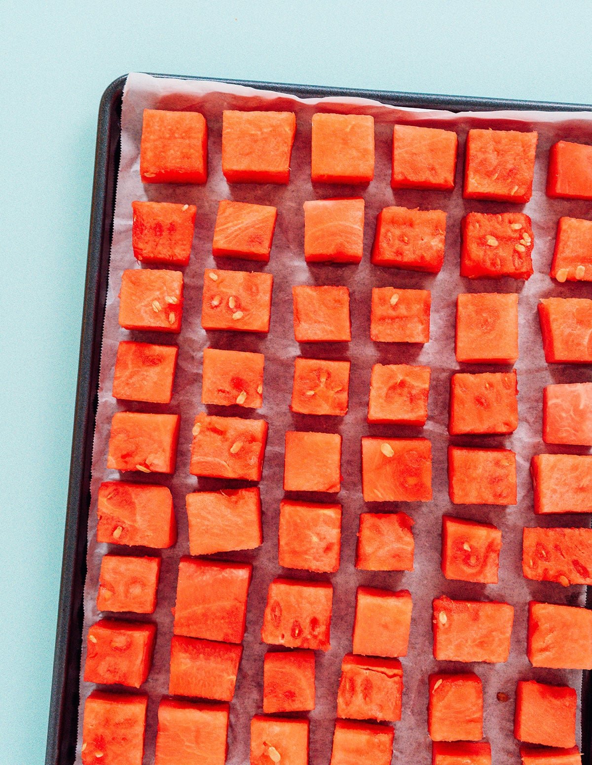 A parchment-lined baking sheet filled with rows of cubed watermelon.