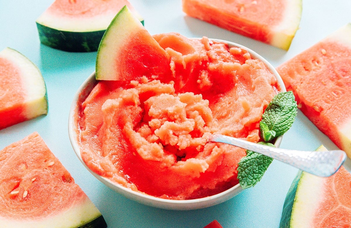 A white bowl of watermelon sorbet with a sliver spoon.