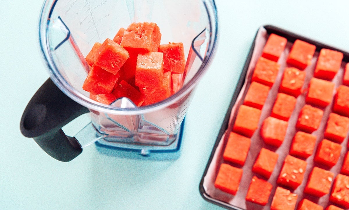 Watermelon cubes on a baking sheet next to some in a blender jar.